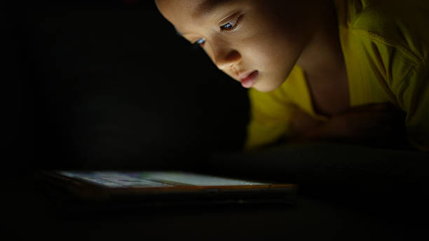 istock Focused child engages with tablet in dimly lit room, showcasing curiosity and concentration. soft glow from screen highlights child features, creating intimate atmosphere 2226452067