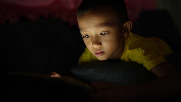 istock Young child is intently focused on tablet screen in dimly lit room, showcasing curiosity and engagement. soft glow from device highlights child features, creating warm and intimate atmosphere 2226452076