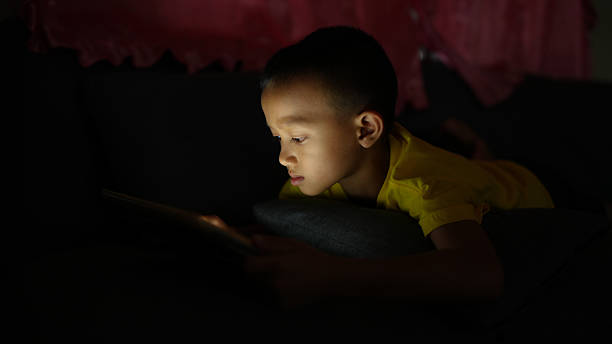 istock Young child is engrossed in tablet, lying on couch in dimly lit room. soft glow from device illuminates child focused expression, creating serene atmosphere 2226452091