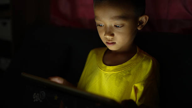 istock Young child is focused on tablet screen, illuminated by its light, wearing bright yellow shirt. scene conveys curiosity and engagement in cozy, dimly lit environment 2226452098
