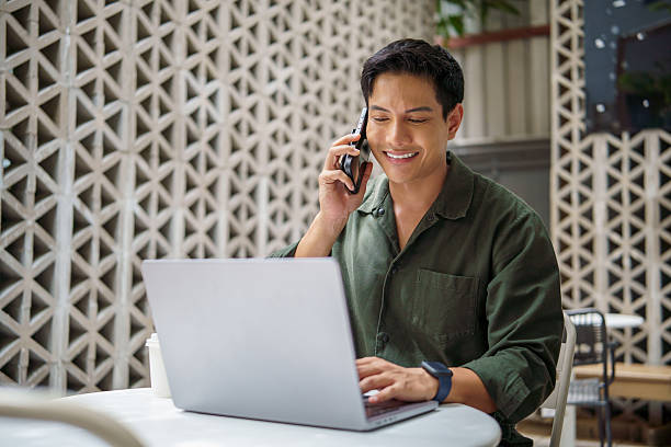istock Smiling businessman talking on the phone while working on a laptop in modern outdoor workspace. 2226456156