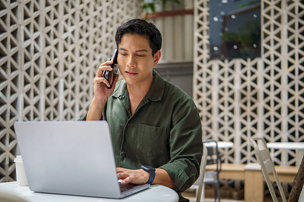 istock Smiling businessman talking on the phone while working on a laptop in modern outdoor workspace. 2226456157