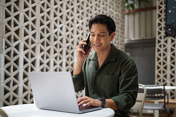 istock Smiling businessman talking on the phone while working on a laptop in modern outdoor workspace. 2226456158