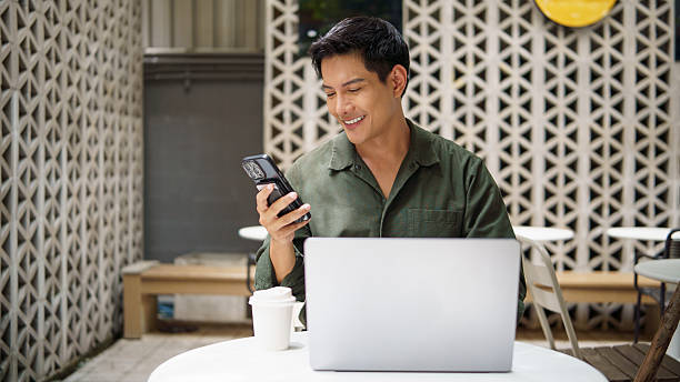 istock Smiling businessman using smartphone while working on laptop at an outdoor cafe. 2226456176