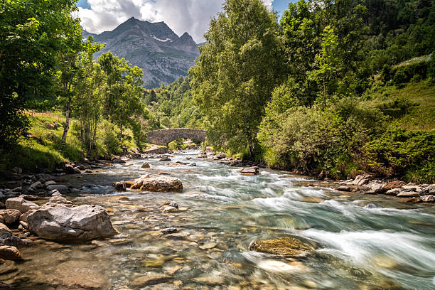 The Gave de Gavarnie river cascades down from the Cirque de Gavarnie through an ancient stone bridge in the French Pyrenees
