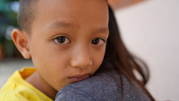 istock Young boy with serious expression is resting his head on person shoulder, showcasing moment of comfort and connection. background is softly blurred, emphasizing emotional bond 2226460107