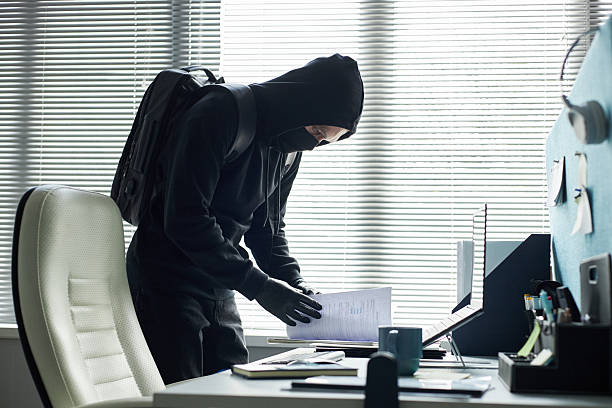 istock Young Caucasian Man Wearing Mask Stealing Documents from Office Desk 2226466637