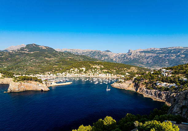 Scenic view of Port de Soller Bay with numerous yachts, boats anchored in turquoise waters. Picturesque Mediterranean coastal scene surrounded mountains, charming waterfront buildings