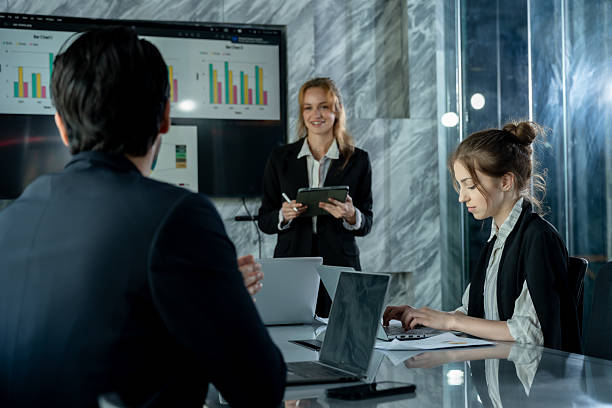 istock Caucasian female leader using digital tablet presenting graphs during business meeting, multiracial colleagues seated at table with laptops sharing ideas and collaborating in modern conference room 2226469921