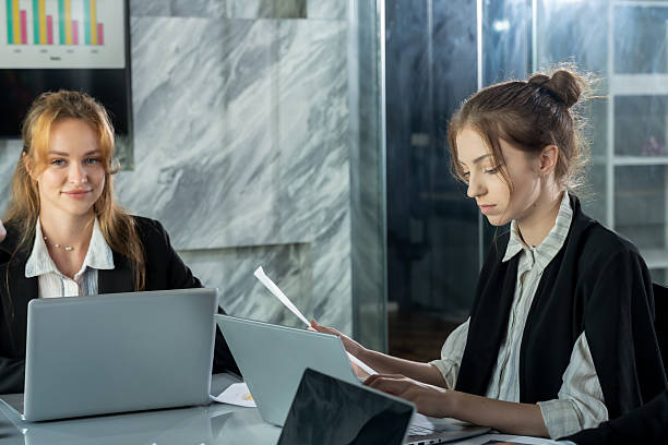 istock Caucasian young female professional reading financial documents and typing on laptop during business meeting, teamwork in office space showing dedication and focus on planning and collaboration 2226469971