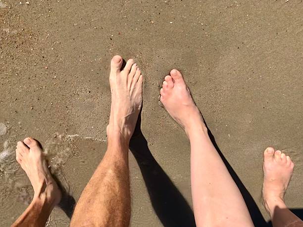 Male and female legs and feet forward in the sand on the beach