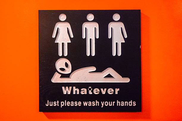 Close-up of unisex bathroom sign against red wall with symbols for male, female, and transgender. With message reading \