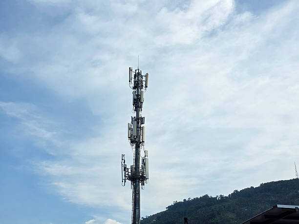 istock Telecommunication tower with multiple antennas and transmitters standing tall against a blue sky with clouds,  and hills in the background. 2226473674