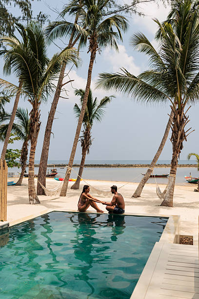 istock Smiling couple talking by the pool with tropical beach in the background 2226474861