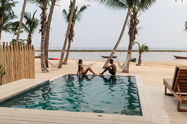 istock Smiling couple talking by the pool with tropical beach in the background 2226474976
