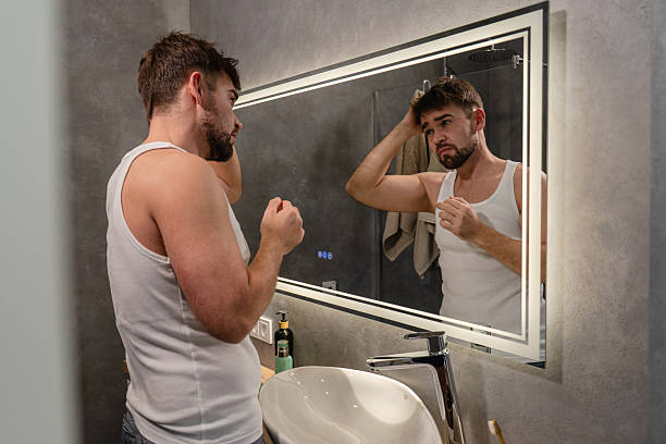 istock Tired-looking man in tank top examining himself in the bathroom mirror 2226475233
