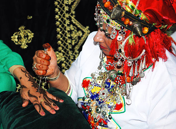Well adorned berber female artist  applying a traditional Henna tattoo on a female hand. This is part of a large showcase of cultural arts of the Desert that takes place every year during the Moussem Festival of Tan Tan in Southern Morocco.\nIn Amazigh (Berber) culture, henna transcends mere decoration; it embodies a significant tradition, linking individuals to their heritage and serving as a beautiful representation of life's cherished moments.