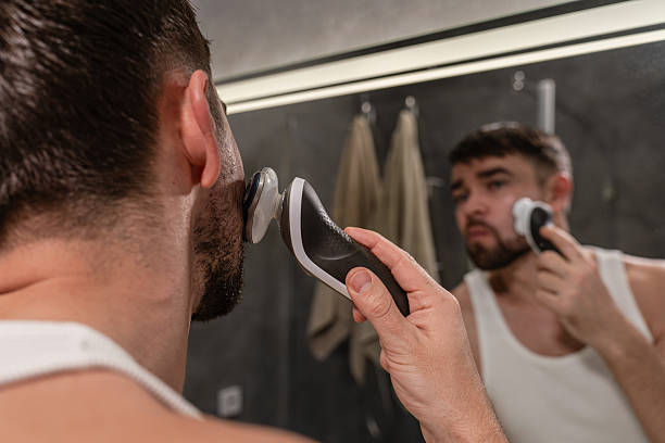 istock Man shaving his face with a rotary electric razor while looking into a mirror 2226475923