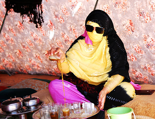 Woman dressed in beautiful berber clothings making mint tea inside a traditional jaima tent.\nThe Berber tea ceremony is more than just making and drinking tea. It represents a rich social tradition, a gesture of hospitality, and a way to build personal relationships. \n\nThis is part of the celebrations of cultures and lifestyles of the desert of the Festival Moussem of Tan Tan that takes place every spring in the southern city of Morocco.