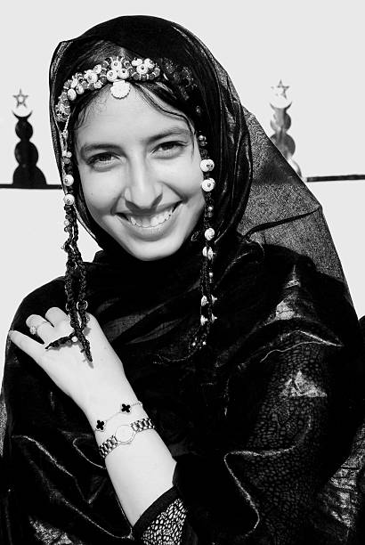 Cute and happy tuareg woman dresssed with traditional sahraui melhfa clothings during a parade at the moussem festival in the city of Tan Tan.\nThe Tan-Tan Moussem Festival is a vibrant celebration of Bedouin culture in Morocco . This festival unites different aspects of Bedouin traditions with a diverse program of music, art, and cultural activities, showcasing the rich desert heritage.\nIt has been acknowledged by UNESCO as part of the Intangible Cultural Heritage of Humanity.