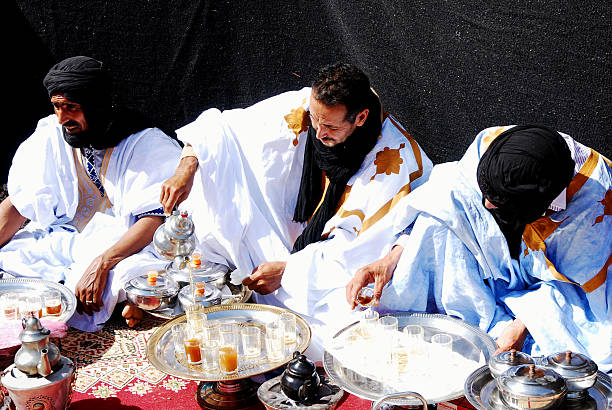 Three men dressed in beautiful berber clothing making mint tea inside a traditional jaima tent.\nThe Berber tea ceremony is more than just making and drinking tea. It represents a rich social tradition, a gesture of hospitality, and a way to build personal relationships. \n\nThis is part of the celebrations of cultures and lifestyles of the desert of the Festival Moussem of Tan Tan that takes place every spring in the southern city of Morocco.