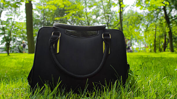 An elegant black women's handbag placed on the grass in a park