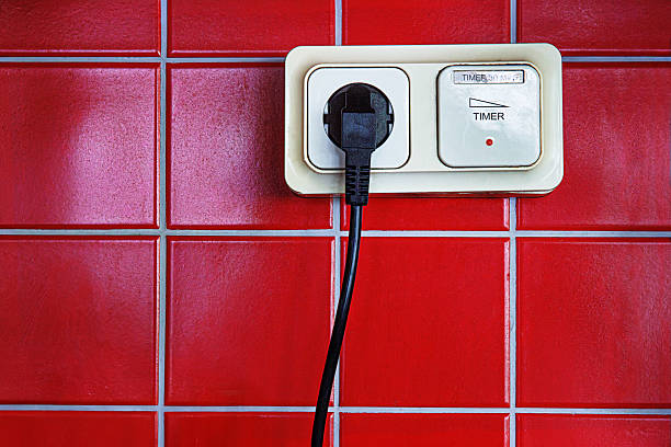 istock A closeup of a black electrical plug inserted into a beige timer switch outlet mounted on a red tiled wall. 2226479224