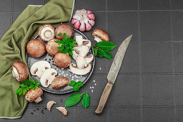 istock Fresh brown mushrooms with garlic, herbs and rustic knife on black tile kitchen surface 2226489795