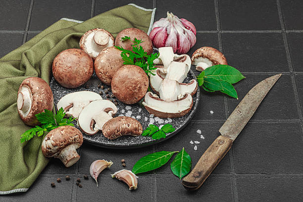 istock Fresh brown mushrooms with garlic, herbs and rustic knife on black tile kitchen surface 2226489796