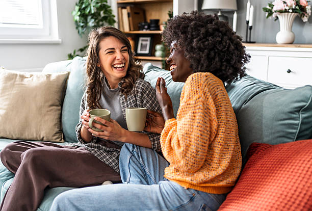 istock Two female friends laughing and drinking coffee on sofa at home 2226495523
