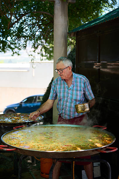 An experienced chef prepares a traditional paella, outdoors, in a Spanish village. The setting reflects a festive holiday celebration where locals gather to enjoy the authentic dish.