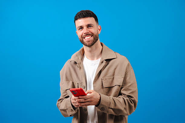 istock Smiling bearded man holding red smartphone against blue background 2226495698