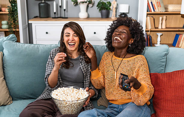 istock Two female friends laughing while watching tv and eating popcorn 2226496073