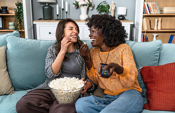 istock Two female friends laughing and eating popcorn while watching tv 2226496222