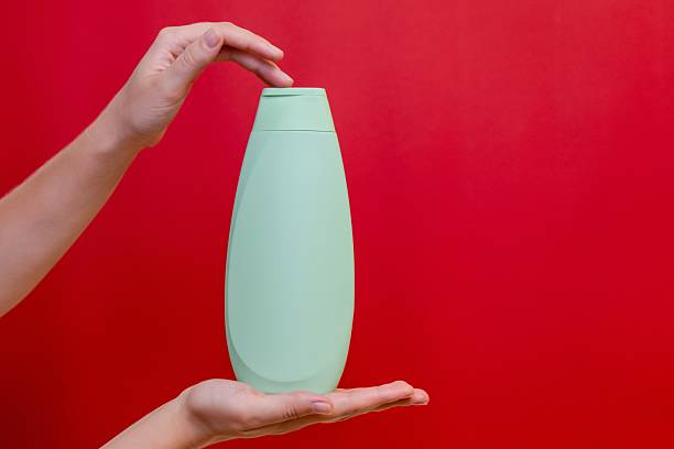 istock Hand with shampoo light bottle isolated on solid red background. Package for cosmetics product, your brand, spa, beauty. Space for text 2226497992