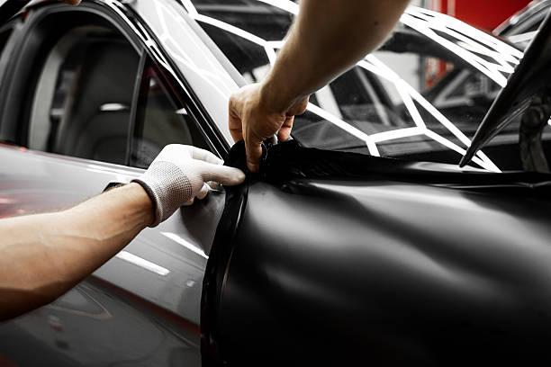istock Full Panel Car Vinyl Wrapping. Large-scale vinyl wrap installation transforms the vehicle exterior with matte black film. Car wrap application changes vehicle appearance. 2226498640