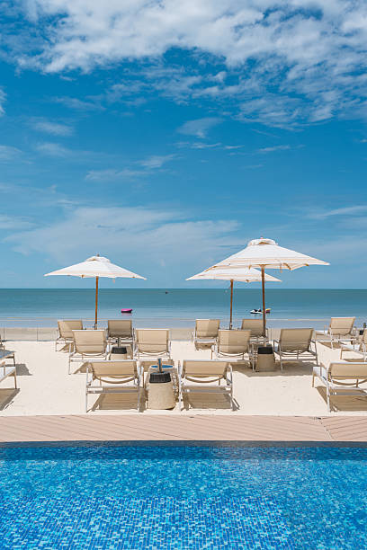 Beachfront resort with poolside, lounge chairs and white parasol on sunny day