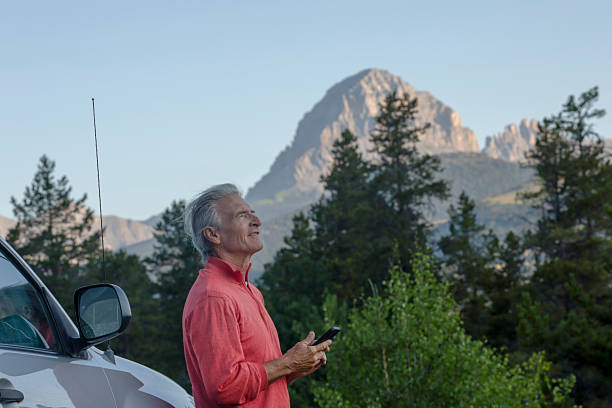 istock Mature man leans against vehicle with mobile phone, mountain peak distant 2226513363