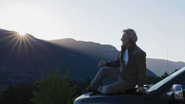istock Mature man relaxes on vehicle at sunrise, mountain distant 2226513436