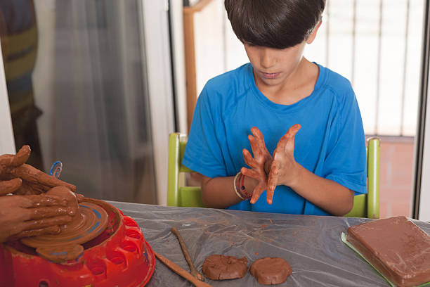 Boy shaping clay with his hands while another child uses a toy pottery wheel. A calm and creative moment at home, ideal for educational or parenting visuals.
