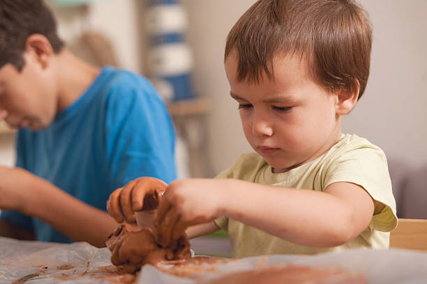 Toddler modeling clay with full concentration beside his sibling. A natural and calm family moment, ideal for educational or parenting use.