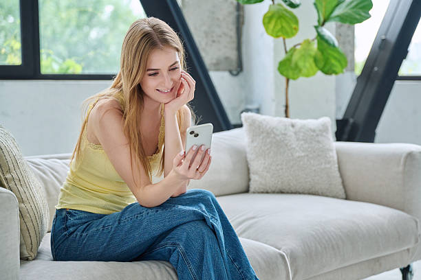istock Young smiling woman sitting at home on couch using smartphone 2226519041