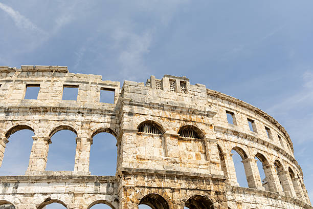 Historic amphitheater structure features weathered stone and arches against a clear blue sky, highlighting architectural beauty and cultural significance