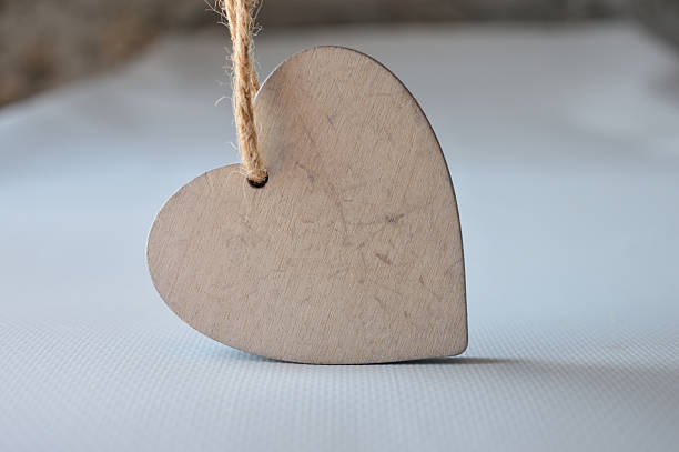 hand holding a plain wooden heart-shaped ornament with a rope loop, blank surface for diy, text, or holiday decoration, isolated on light background