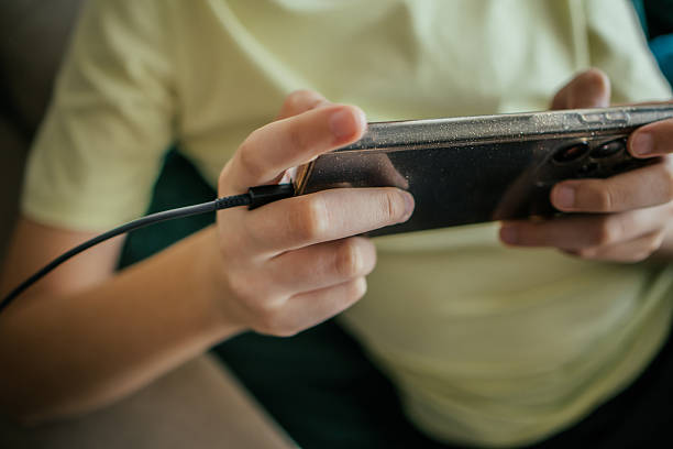 Everyday Electricity. Young boy playing video games on his mobile phone  at home while phone is charging.