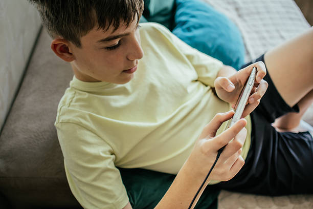 istock Everyday Electricity. Young boy playing video games on his mobile phone  at home while phone is charging. 2226522584
