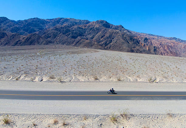 Biker riding motorcycle on mountain road on sunset.