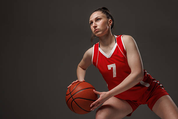 istock Female basketball player in red uniform dribbling and focused in action, isolated on dark studio background 2226523607
