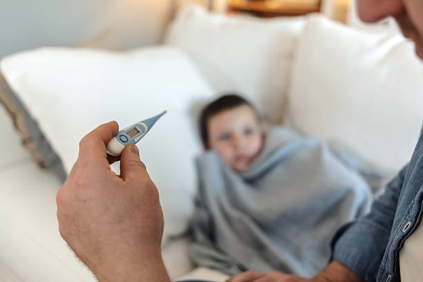 istock Young father checking temperature of sick son lying while lying in bed. Father checking her sick sons temperature. 2226530892