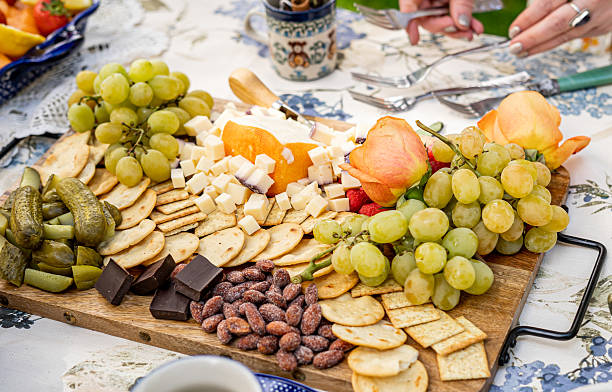 charcuterie board, cheese platter, grapes, crackers, chocolate, nuts, fruit, cheese cubes, assorted snacks, pickles, green grapes, food arrangement, appetizer tray, close up food, gourmet food, snack board, picnic food, entertaining platter, table spread, rose garnish, variety of snacks, wine pairing food, celebration platter, soft cheese, cubed cheese, food and drink, table setting, rustic food, artisan snacks, gourmet presentation, snack display, appetizer assortment, fresh fruit, edible flowers, elegant serving, party platter, social gathering, cheese and fruit, sweet and savory, casual dining, grazing board, alfresco meal